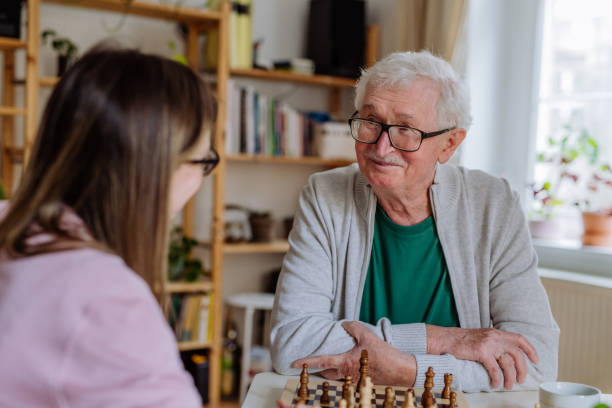 An adult daughter visiting her senior father at home and playing chess together.