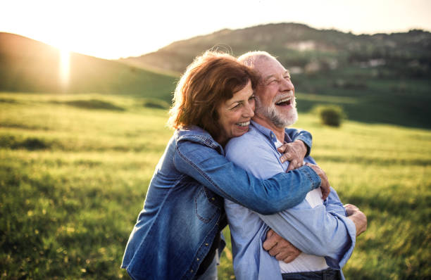 Happy senior couple outside in spring nature, hugging at sunset. Side view.